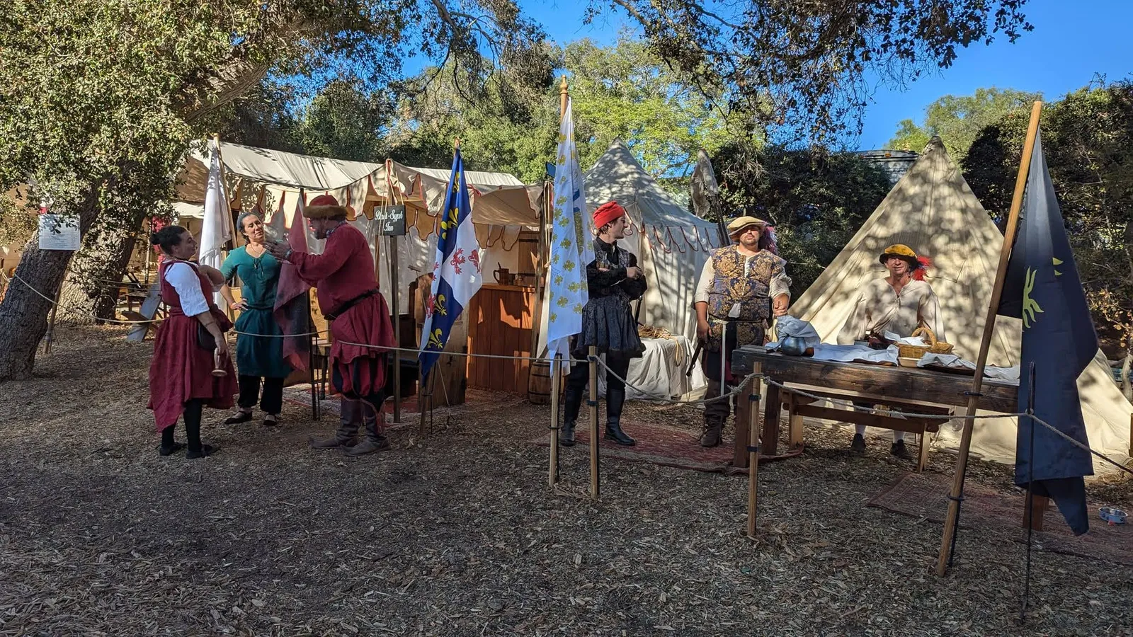 Reenactors gathered among canvas tents and banners in the medieval encampment