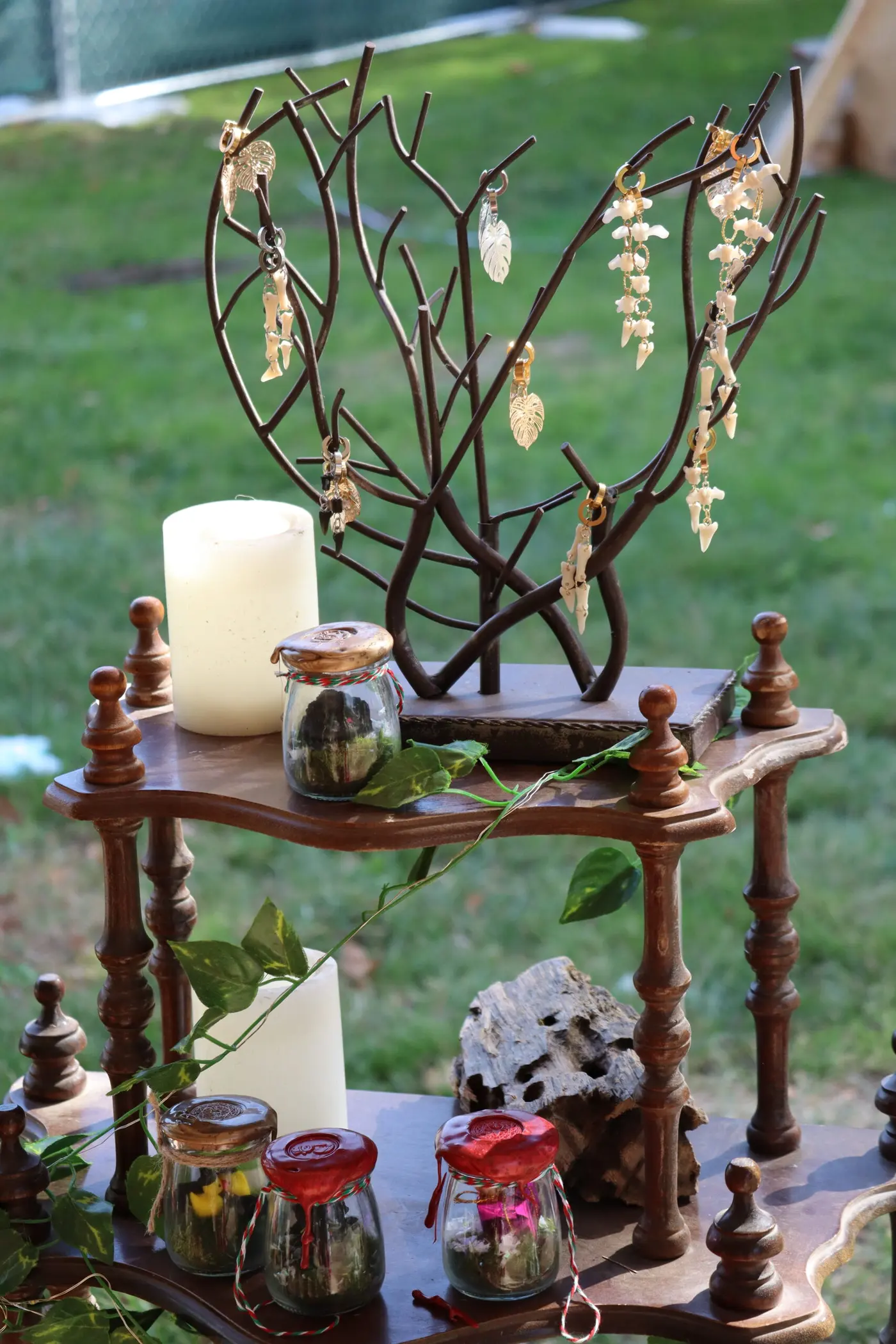 A wooden display shelf with a candle, glass jars and a branch hung with small charms