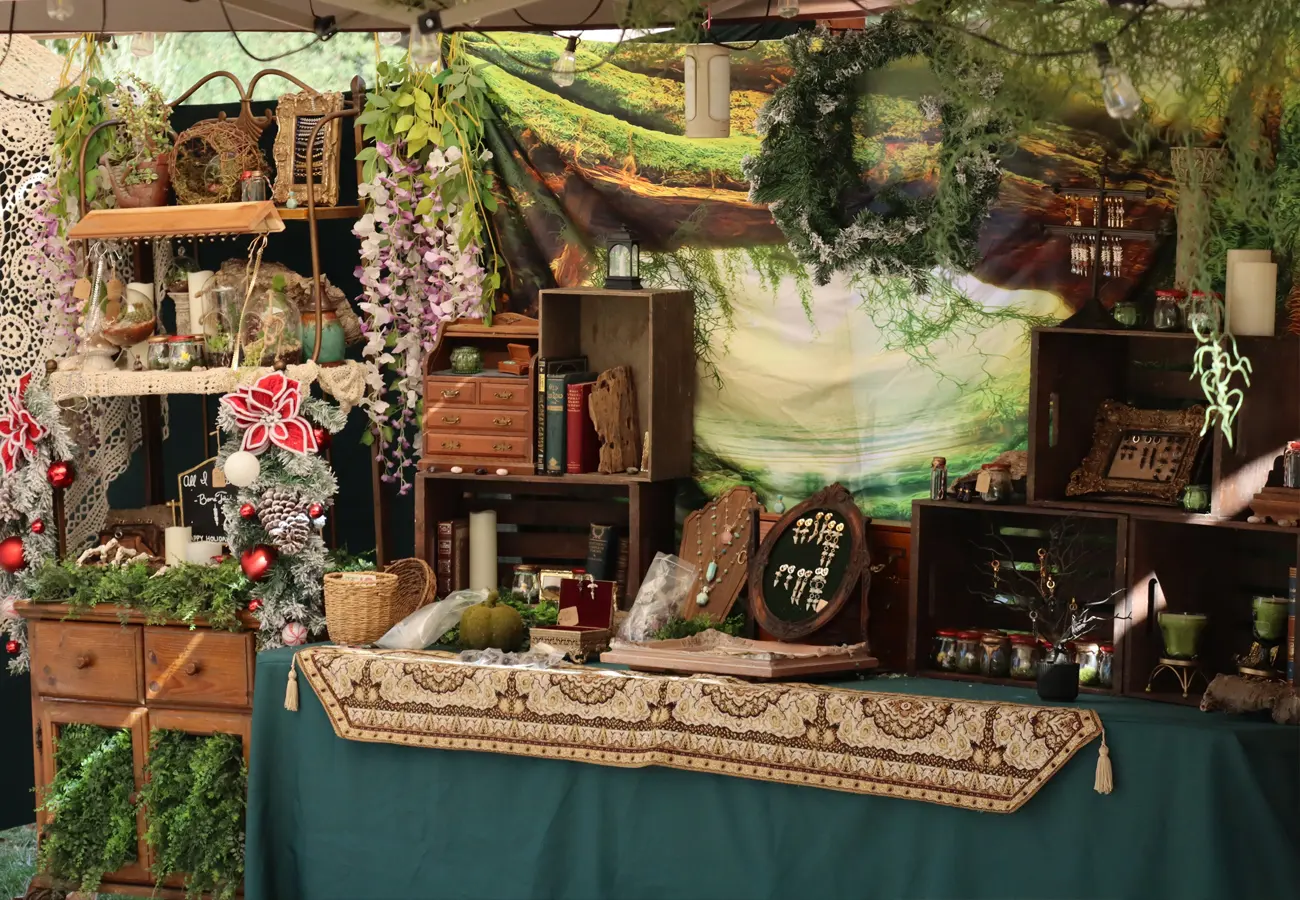 A green-draped artisan booth with shelves of herbs, jars and garlands