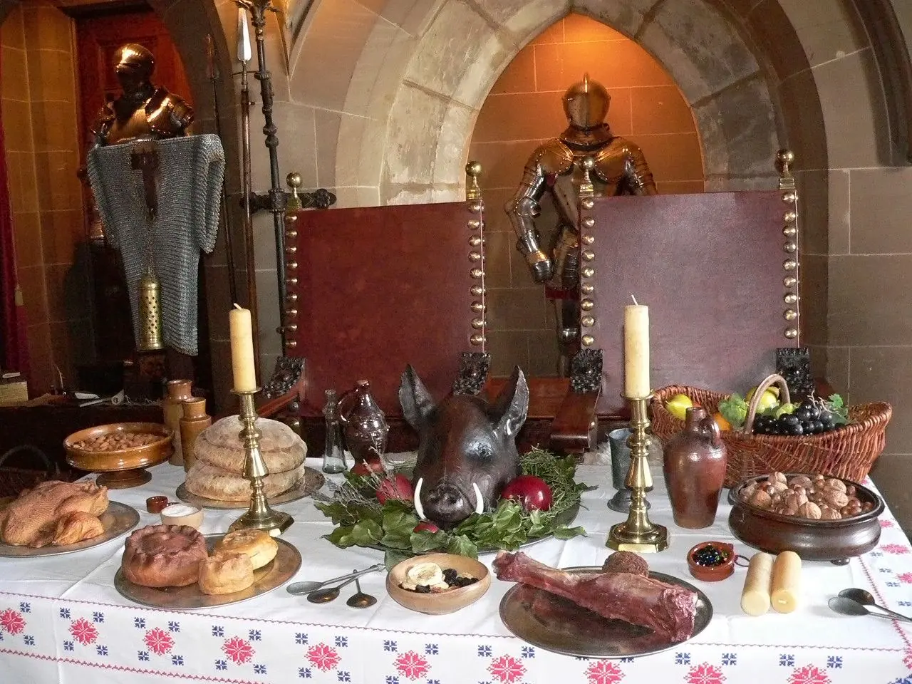 A medieval banquet display of breads, pies, candles and a boar's head beneath suits of armor