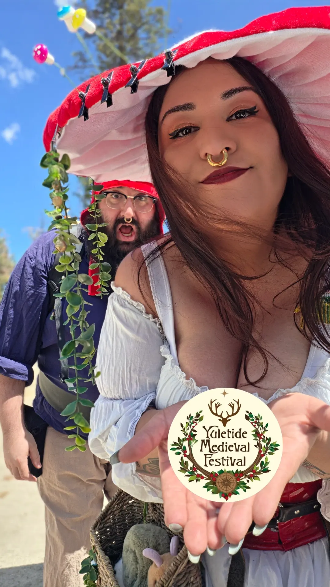 A woman in a red-spotted toadstool hat holds out a Yuletide Medieval Festival token
