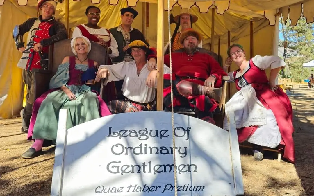 The League of Ordinary Gentlemen company seated in costume behind their painted sign