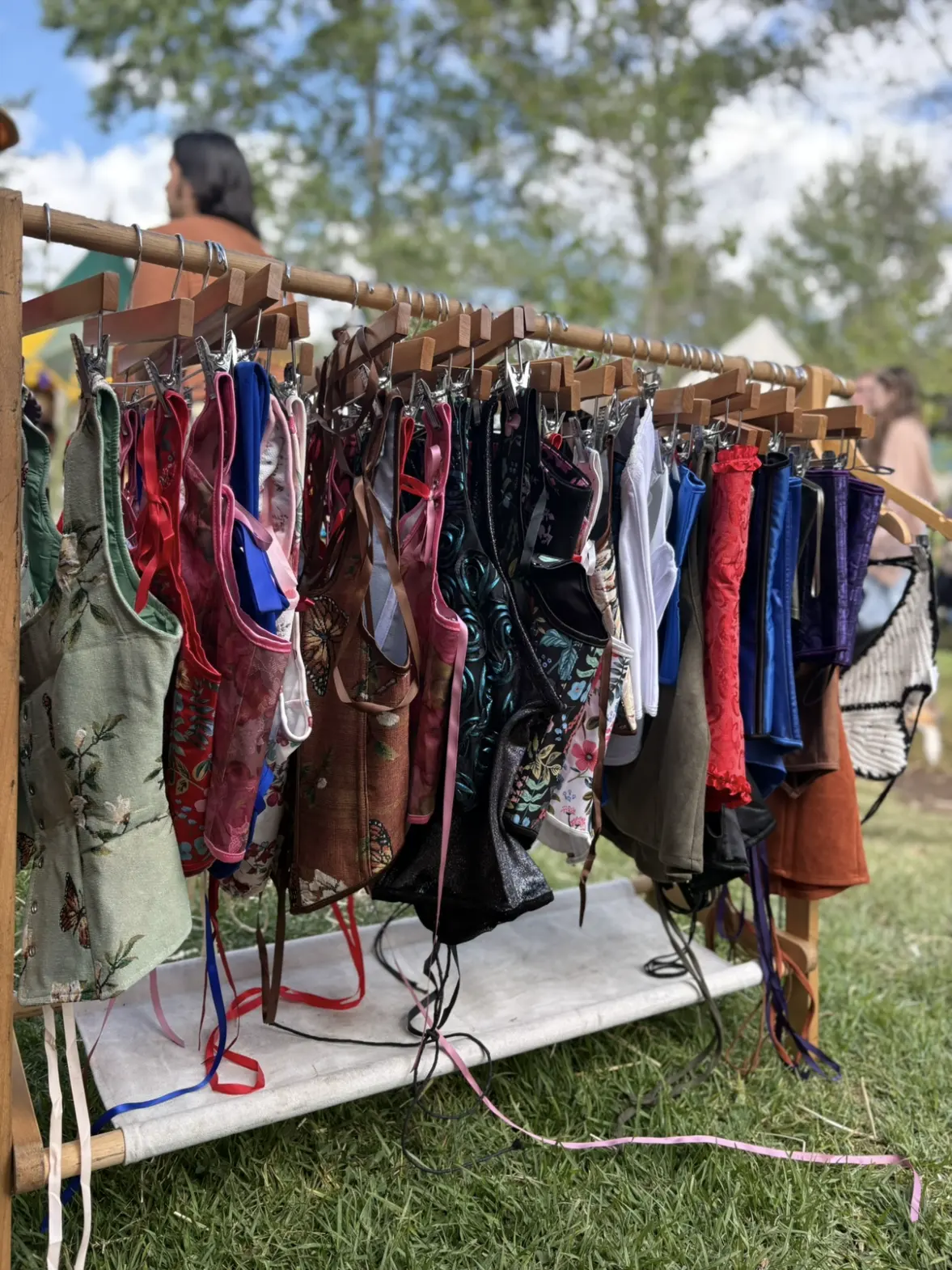 A row of laced bodices and corsets on a wooden clothing rack outdoors