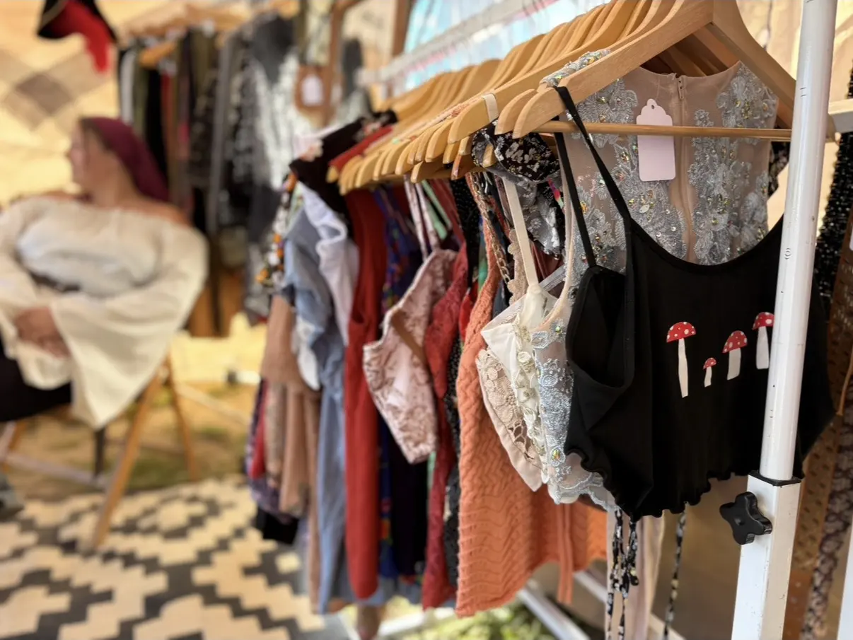 Hanging blouses and chemises at a clothing booth, with a costumed shopper behind