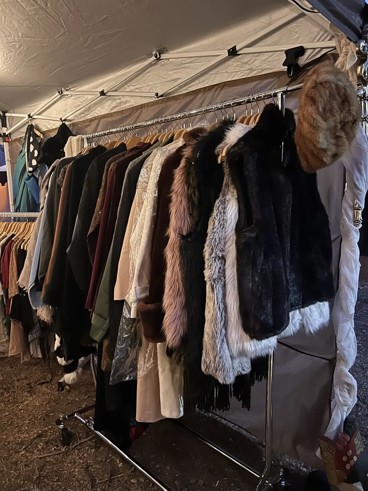 Fur-trimmed coats and vests hanging under a vendor tent