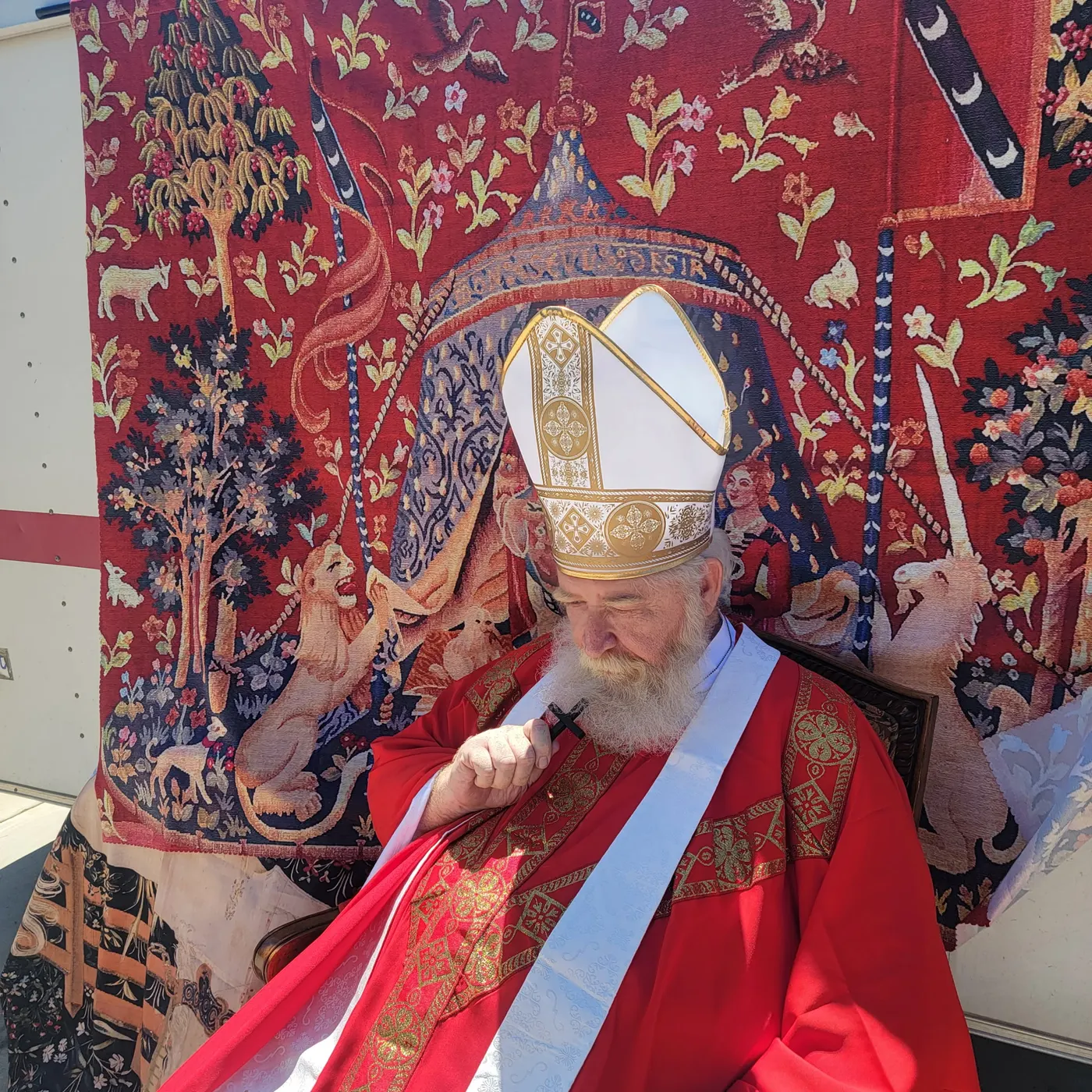 St. Nicholas resting his head on his hand before a red unicorn tapestry