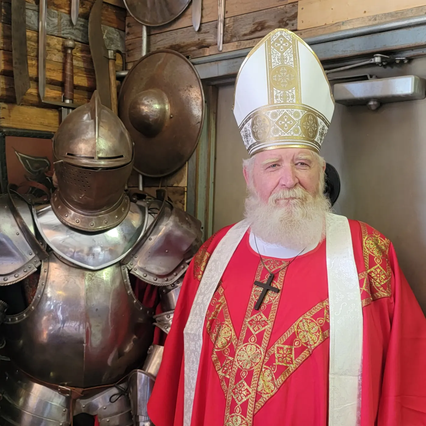 St. Nicholas smiling beside a suit of armor and round shields on a wooden wall