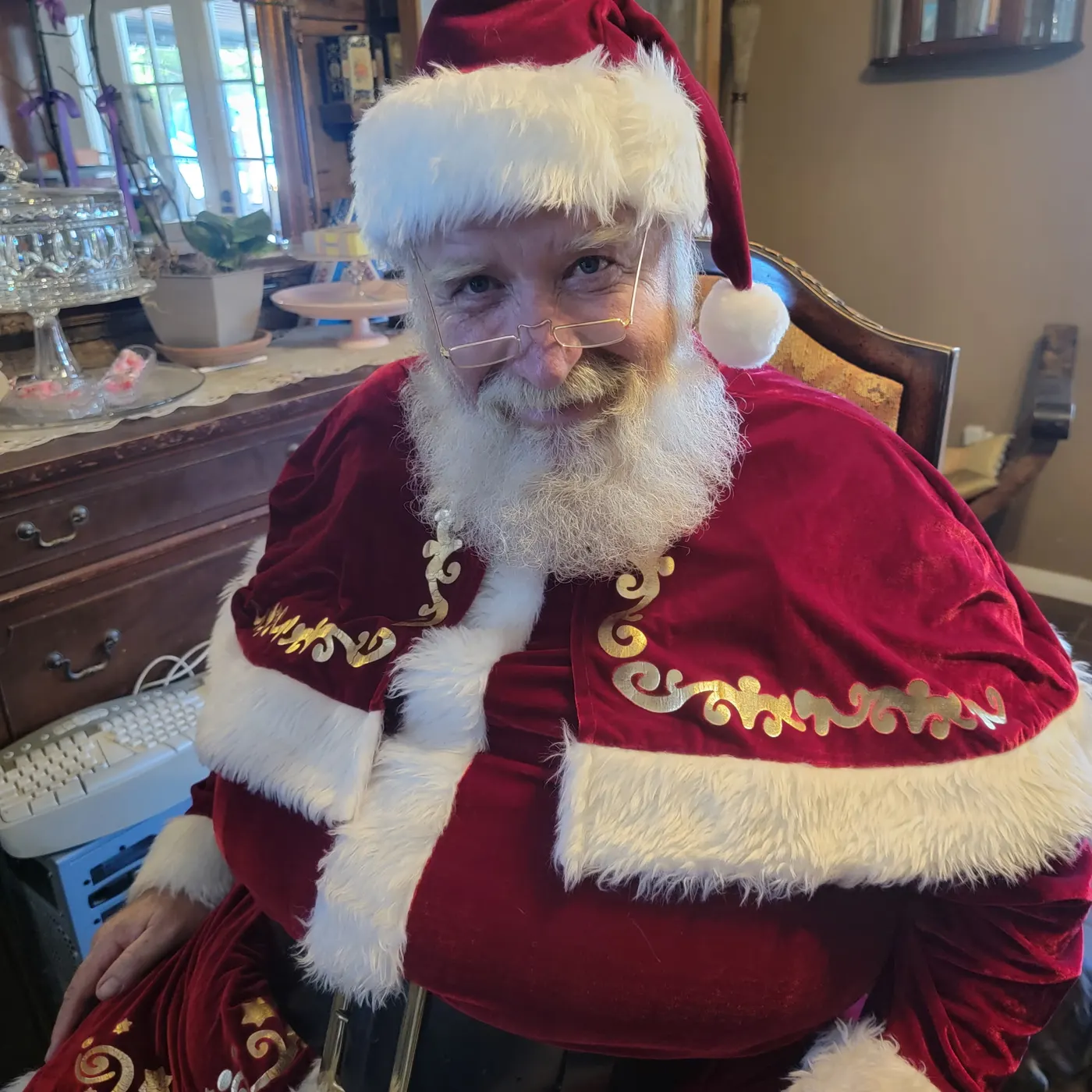 Father Christmas in red velvet with white fur trim and gold scrollwork, smiling in a carved chair
