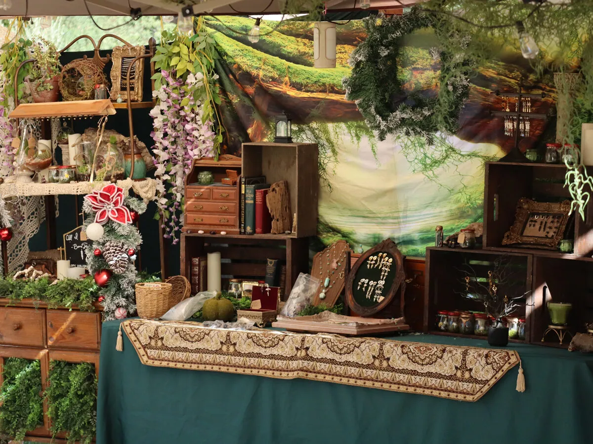 An artisan shop booth dressed with greenery, wooden shelves and handmade goods